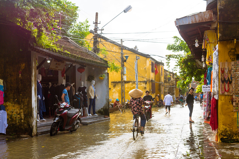 Woman biking through the rainy streets of Hoi An. Historic Flooding in Hoi An