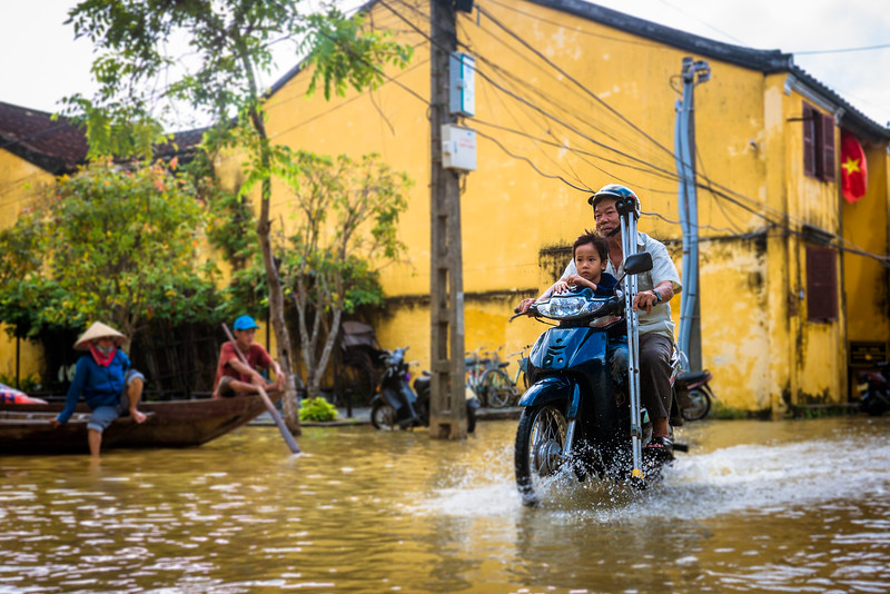 A dad and son make their way through the flooded city. Dad on motorbike sustainable issues hoi an