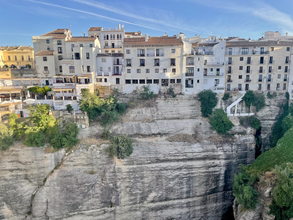 Wide view of white and tan buildings stacked along the edge of El Tajo gorge in Ronda.