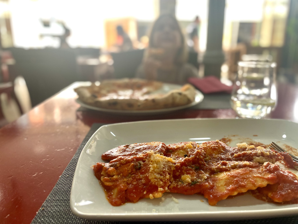 Close-up of a wood-fired pizza and pasta on a plate at a restaurant table.
