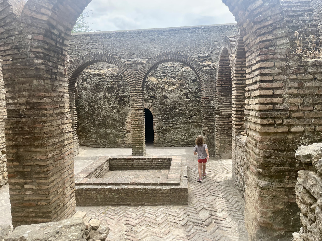 Interior of the Arab Baths in Ronda, showing horseshoe brick arches and a child walking toward the bathing pool.