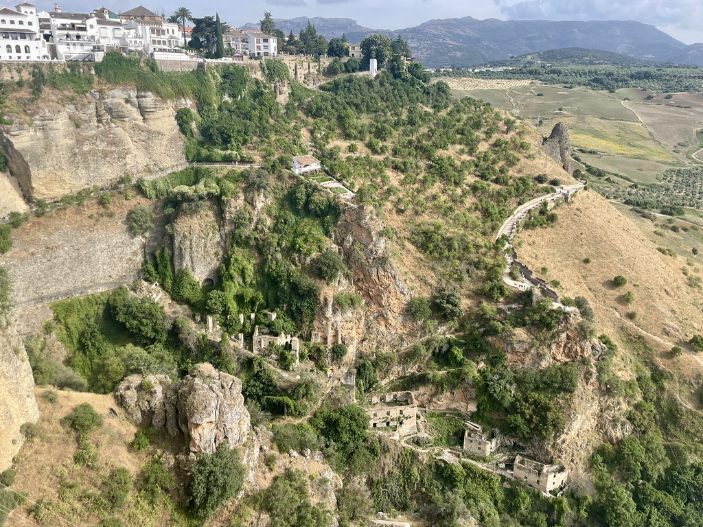 Wide aerial view of Ronda perched on a cliff above El Tajo gorge, showing terraced ruins and surrounding countryside.