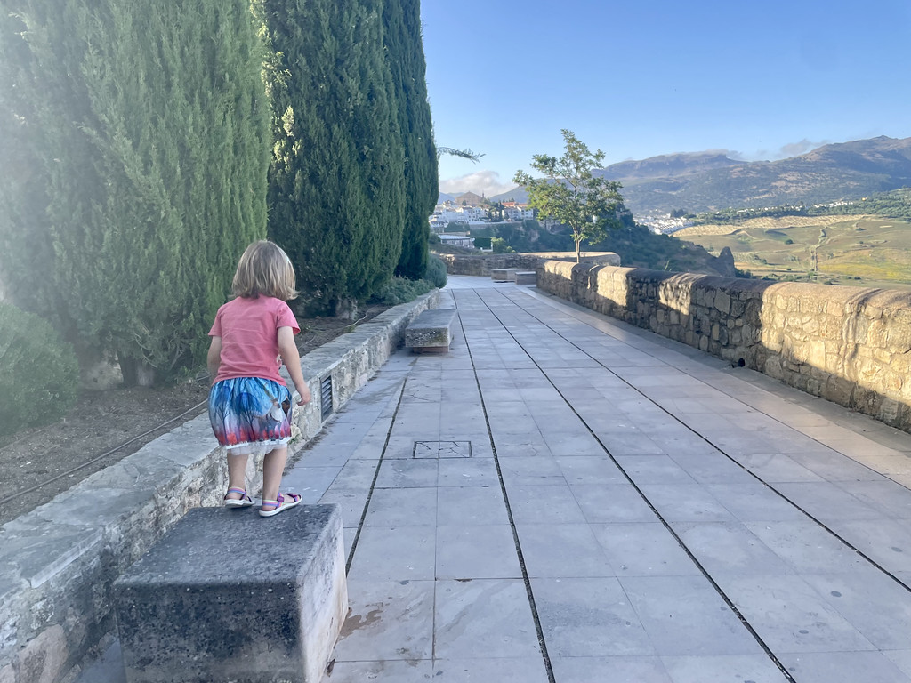 A child standing on a low stone wall along a walking path overlooking the Andalusian countryside.
