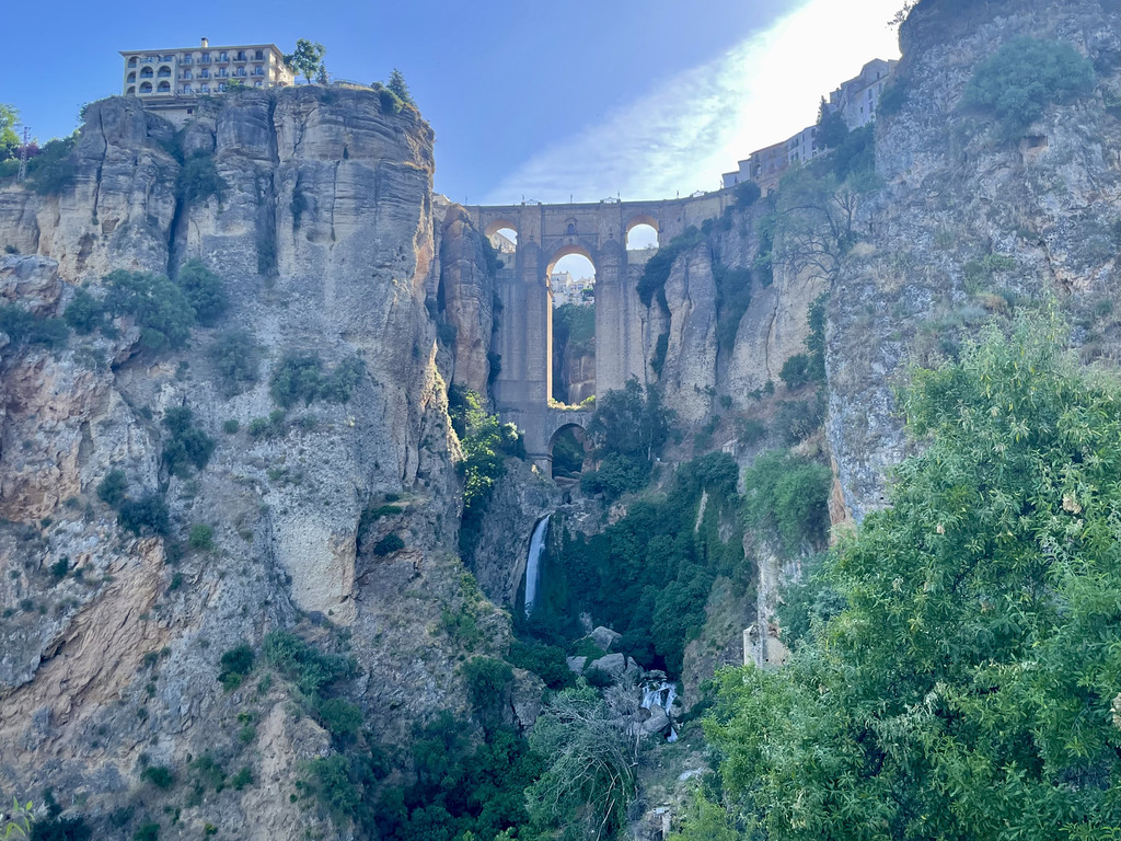 Wide view of Puente Nuevo bridge arching over El Tajo gorge with a waterfall beneath it.