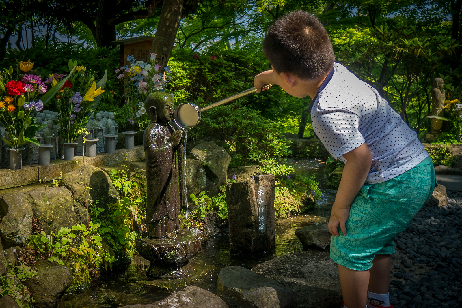 A young boy watched his mother pour water over the Jizō statue, and then poured water in the same manner. worshipping at Jizō Hase-dera Temple in Kamakura, Japan