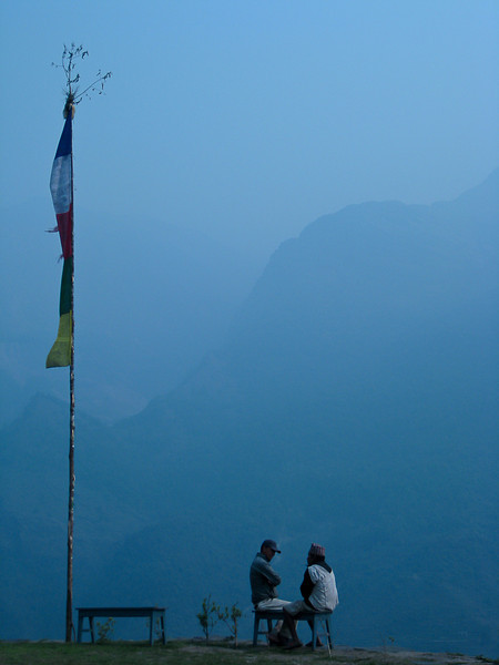 Two men quietly talk in the early evening high in a town we paused in for mere minutes while I hiked along the Annapurna circuit in Nepal Trekking in Nepal there are locals living along the way who just go about their business.