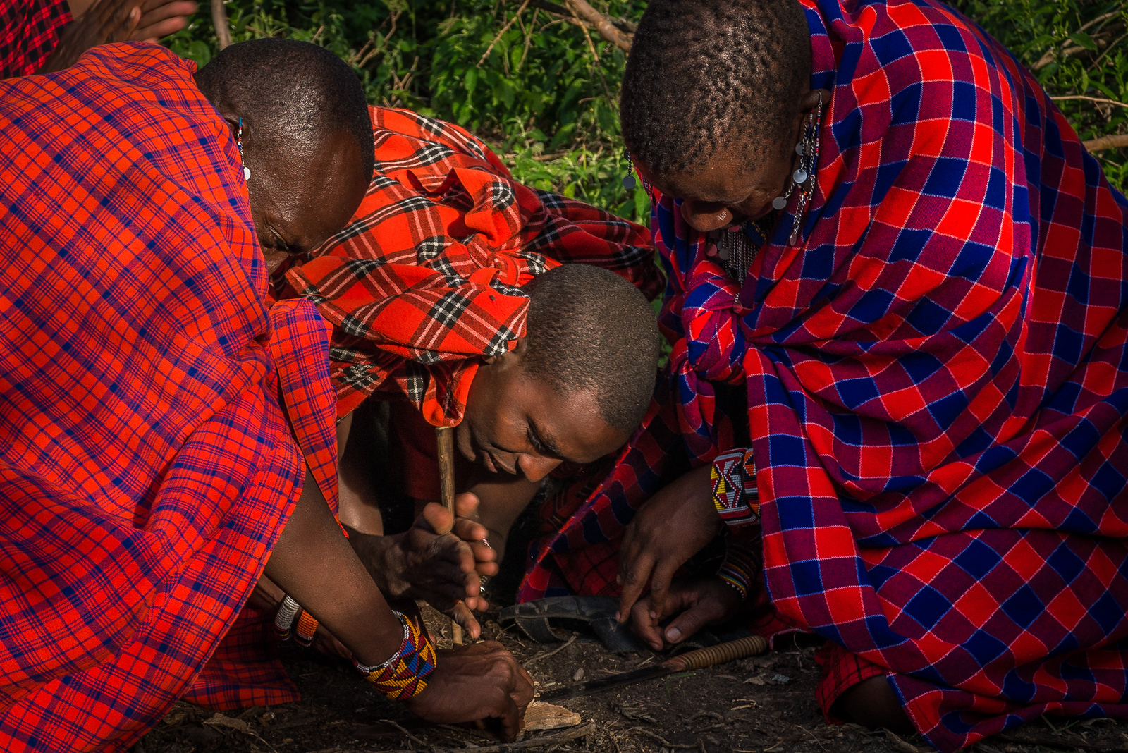 The men all took turns so that they could keep the heat and friction building as they spun the stick in a thin piece of wood that had kindling of leaves and grasses around it. the Maasai lighting a fire by hand